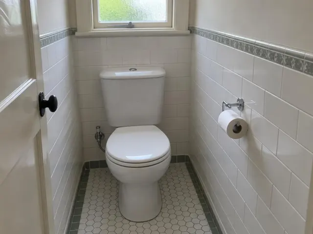 Clean toilet in a small tiled bathroom with a window above in Bexley